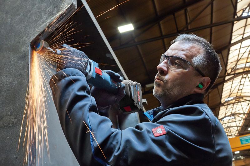 一名佩戴安全设备的人研磨金属，产生明亮的火花。.