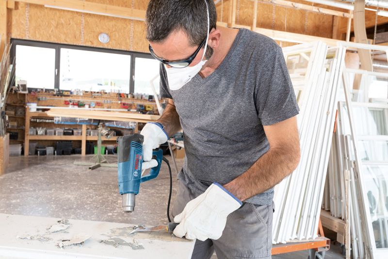 一名佩戴安全设备的人员使用热风枪去除表面的油漆。