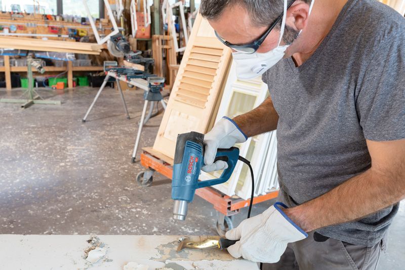 一名佩戴安全设备的人员使用热风枪去除木质表面的油漆。