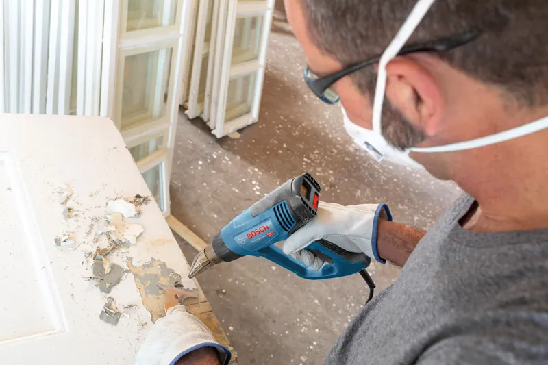 佩戴安全设备的人员使用热风枪剥去门上的油漆。