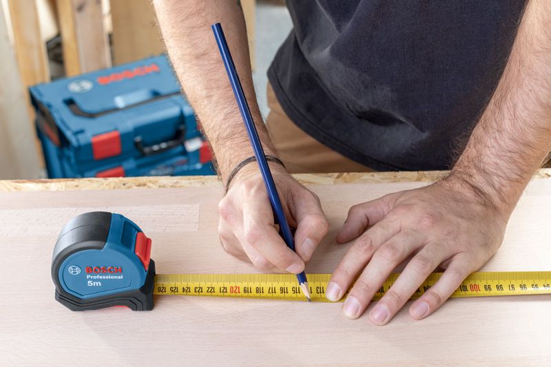一个人用卷尺和铅笔在木头上标记测量值。.