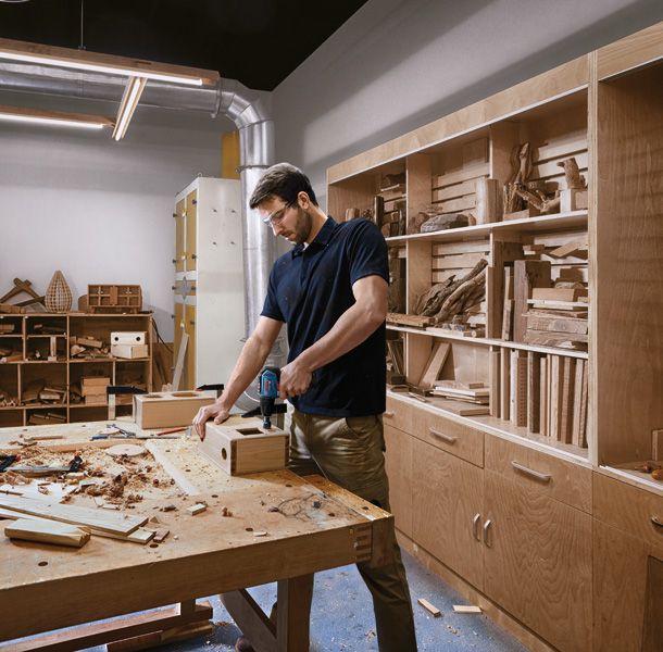 一名佩戴安全设备的人员在车间使用无绳电钻对木箱进行钻孔。.