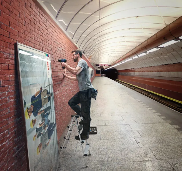 一名男子使用无绳电钻在地铁站的砖墙上安装框架。.