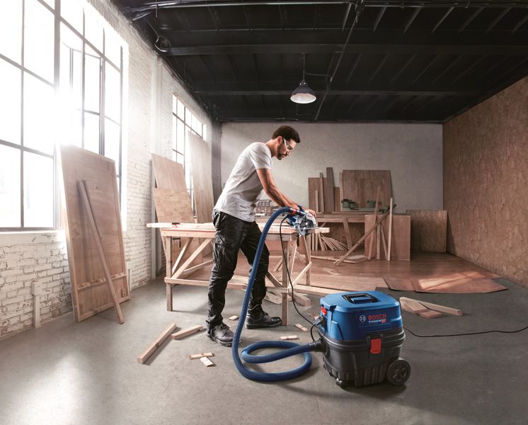 一名佩戴安全设备的人员在木材车间使用吸尘器。.