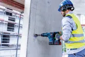 一名佩戴安全装备的人员使用无绳电锤在混凝土上钻孔。