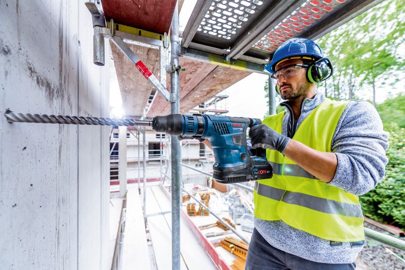 一名佩戴安全装备的人员使用无绳电锤钻入混凝土。