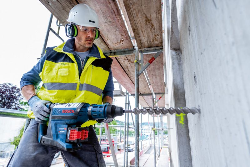 一名佩戴安全装备的人员使用无绳电锤钻入混凝土。