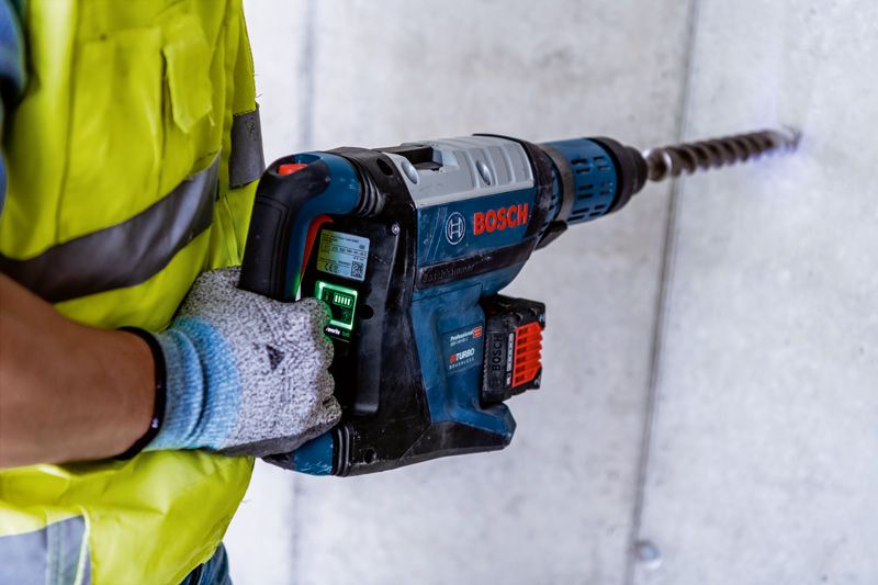 一名佩戴安全设备的人员使用大型旋转锤在混凝土中钻孔。.