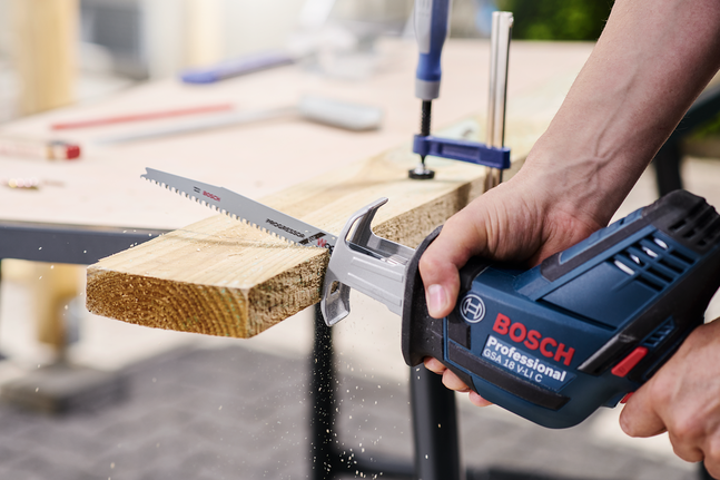 一个人在工作台上用往复锯切割木板。