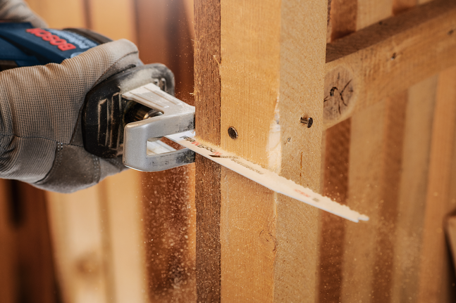 一名佩戴安全装备的人员用往复锯切割木梁。