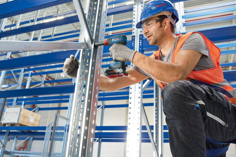 一名佩戴安全设备的人员使用无绳电钻固定金属框架。.