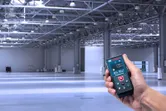 一个人在一个空荡荡的大型工业仓库中使用激光测量仪。.