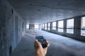 一名男子使用激光测量仪测量未完工混凝土房间内的距离。.
