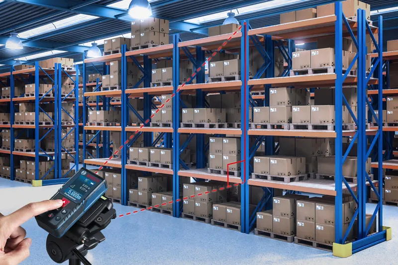 一个人使用激光测量仪检查仓库货架之间的距离。.