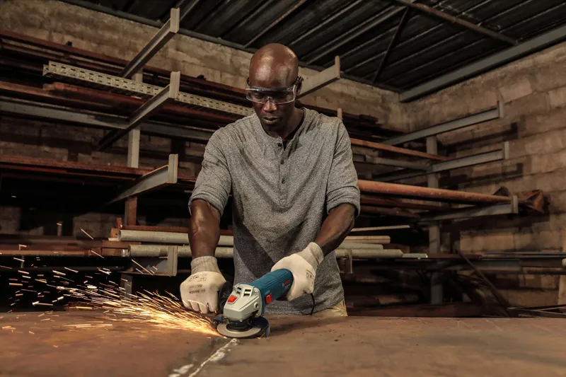 一名佩戴安全设备的人员在车间研磨金属，产生火花。.