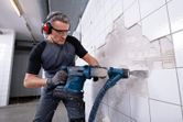 一名佩戴安全设备的人员使用无绳旋转锤拆除墙砖。.