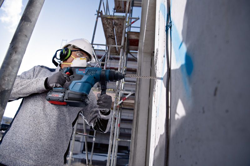 一名戴着安全设备的工人在建筑工地上钻入混凝土墙。.