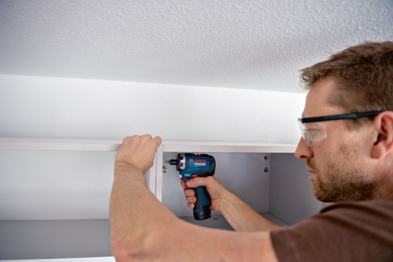 一名佩戴安全设备的人员使用无绳螺丝刀组装橱柜。.