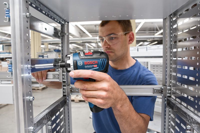 一名佩戴安全设备的人员使用无绳螺丝刀在金属框架上工作。.