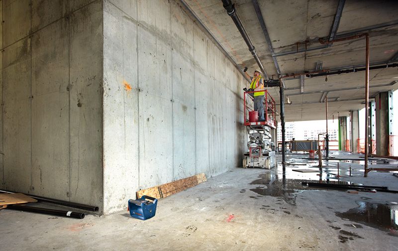 一名佩戴安全设备的人员正在使用激光调平工具对混凝土墙进行调平。.