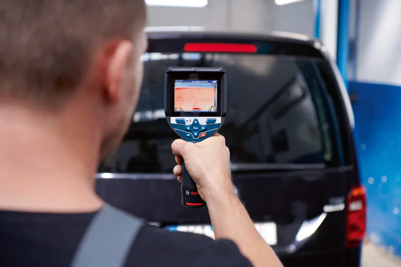 一个人使用热像仪扫描车辆的后窗。.