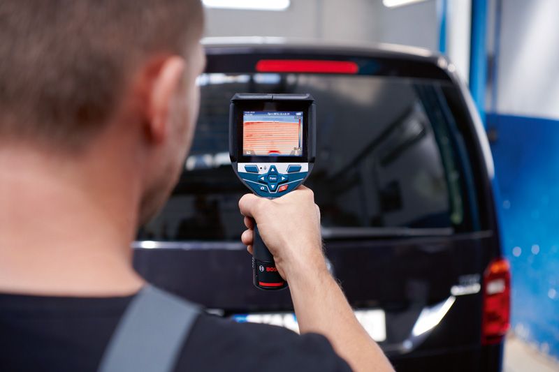 一名男子使用热成像仪扫描一辆黑色厢式货车的后窗。