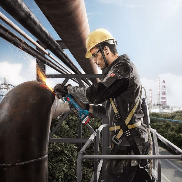 一名佩戴安全设备的人员正在用角磨机打磨一根大型金属管。.