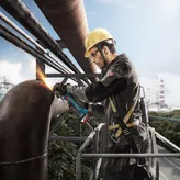 一名佩戴安全设备的人员正在用角磨机打磨一根大型金属管。.