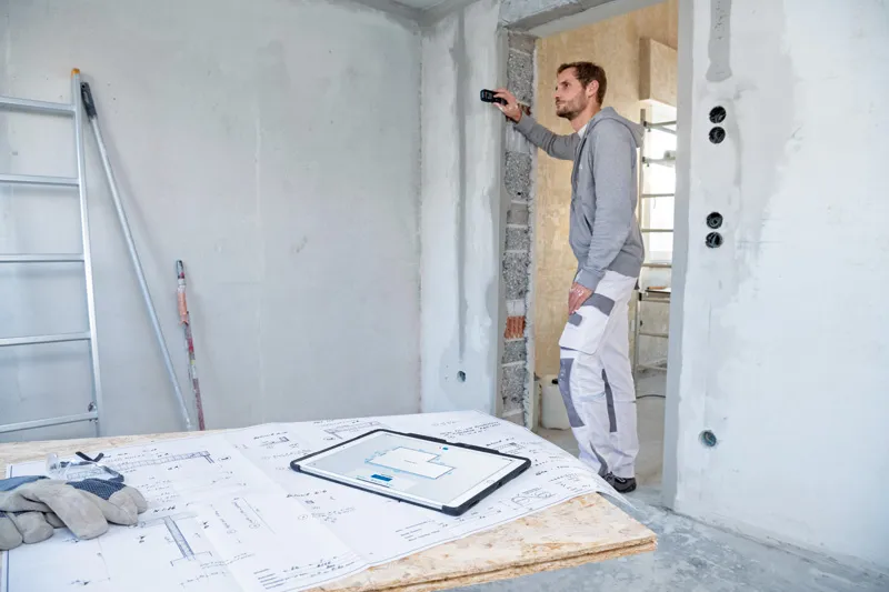 一名工人使用激光测量仪检查建筑工地的墙壁距离。.