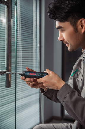 有人用无线螺丝刀将螺丝拧到玻璃门把手上。