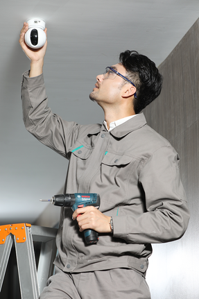 一名佩戴安全装备的人员正在用电钻安装监控摄像头。