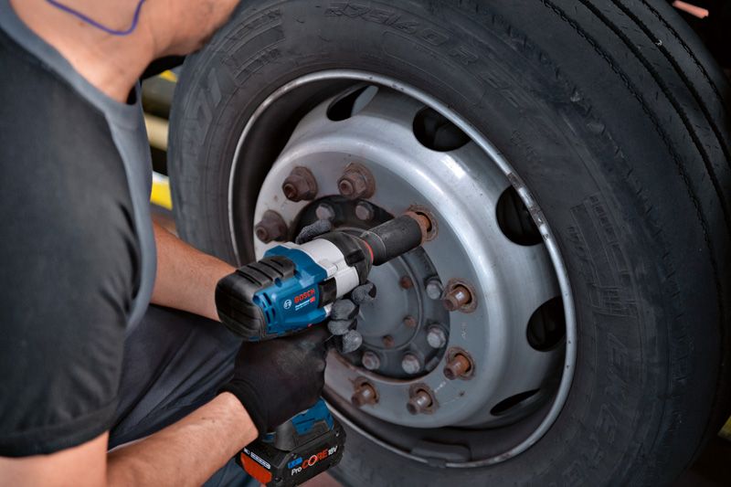 一名佩戴安全设备的人员使用冲击扳手拧紧卡车车轮上的螺栓。.