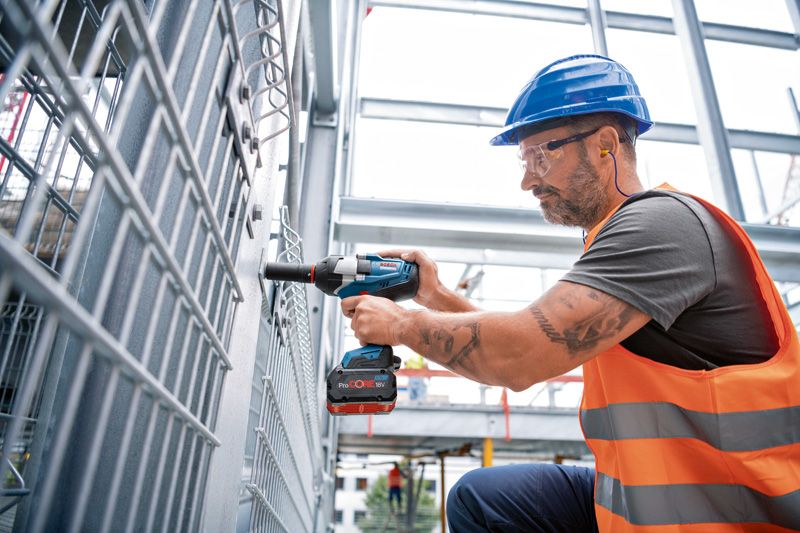 一名佩戴安全设备的人使用无绳冲击扳手撬动金属栅栏。.