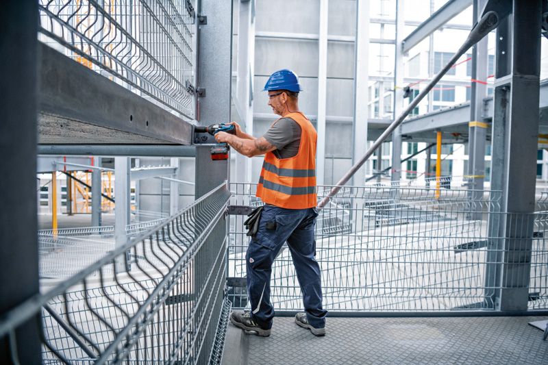 施工现场，一名佩戴安全设备的人员使用冲击扳手拧紧钢梁。.