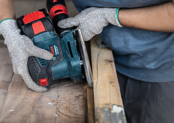 佩戴安全设备的人员使用电动工具打磨木质表面。