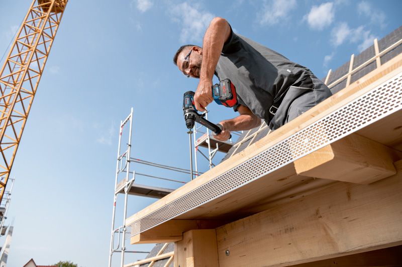 一名佩戴安全设备的人员正在向正在建造的建筑物的木梁上钻孔。.