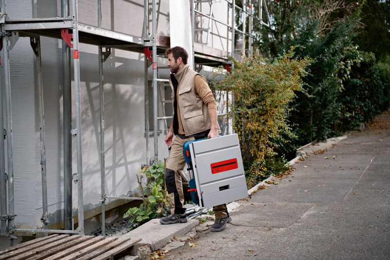 一名佩戴安全设备的人员在建筑工地搬运无绳台锯。