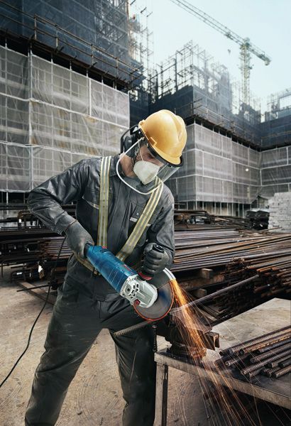 建筑工地上，一名佩戴安全设备的工人正在用角磨机打磨金属棒。.