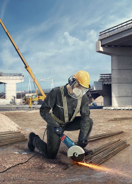 一名佩戴安全设备的人员在建筑工地使用角磨机切割金属棒。.