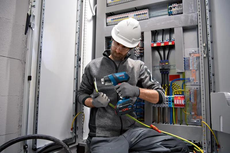 一名佩戴安全设备的人员使用无绳热风枪对电线进行加热。.