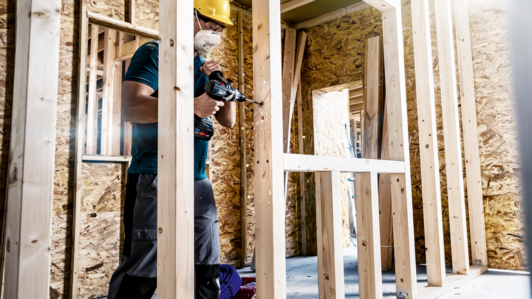 一名佩戴安全设备的人员在建筑工地上钻木框架。