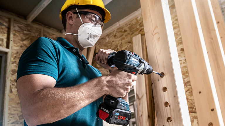 佩戴安全设备的人员在木梁上钻孔。