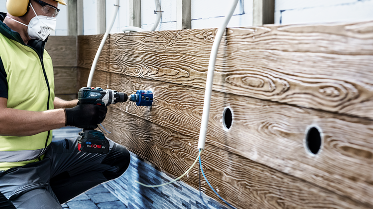 一名佩戴安全设备的人员在木墙上钻了一个大洞。