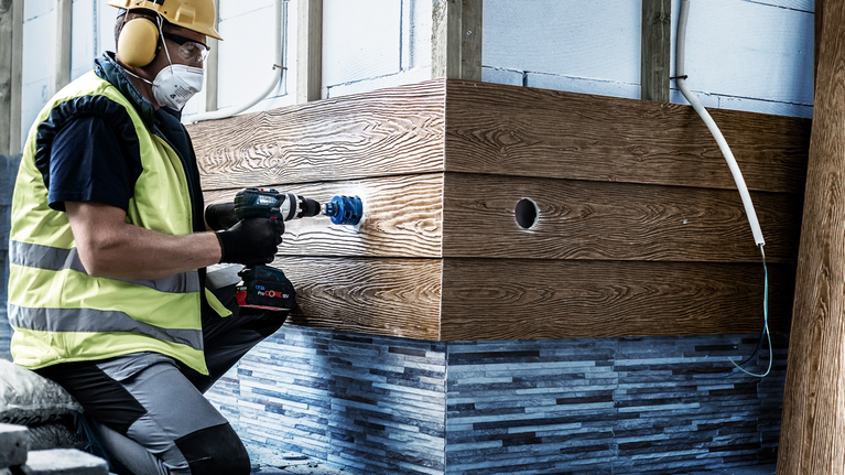 一名佩戴安全设备的人员在木镶板上钻孔。