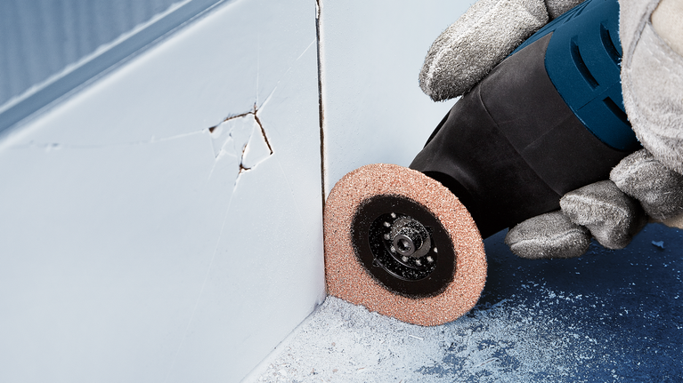 佩戴安全设备的人员使用旋转工具在墙角附近进行打磨。