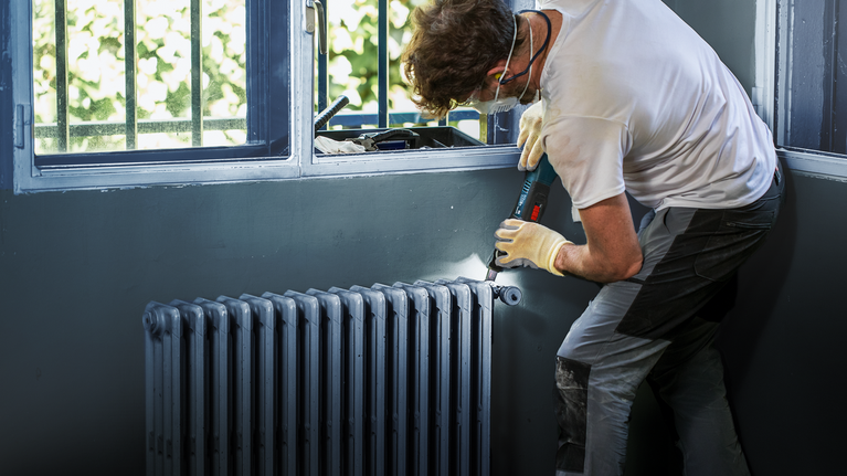 佩戴安全设备的人员使用无绳电钻安装散热器。