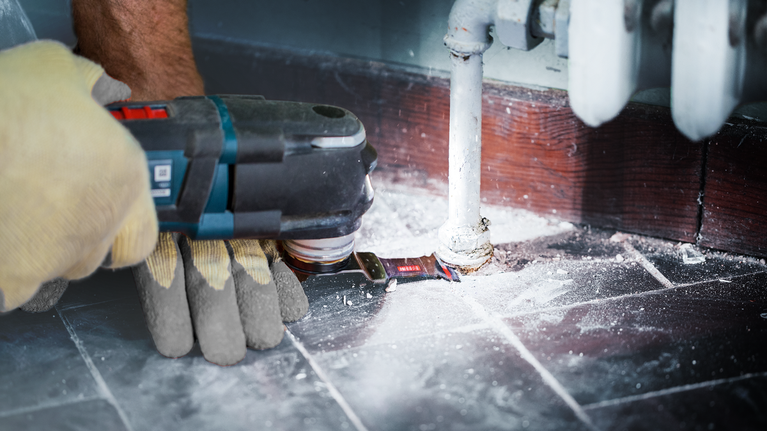 一名佩戴安全设备的人员使用电动工具切割管道周围的地板。