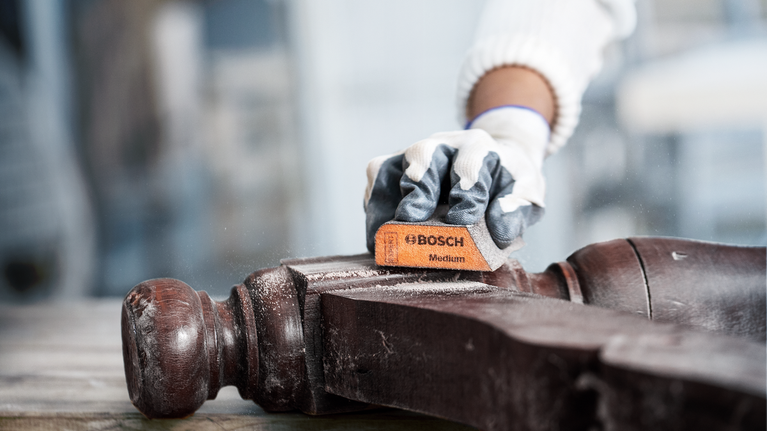 穿着安全设备的人员正在打磨木椅扶手。