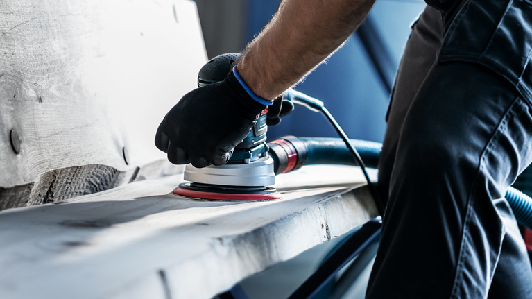 佩戴安全设备的人员使用电动砂光机打磨木板。