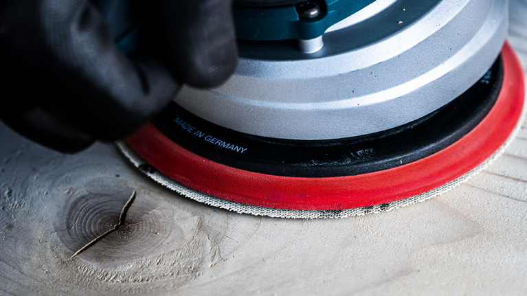 一名佩戴安全设备的人员正在使用电动工具打磨木质表面。